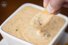 a hand dipping a tortilla chip into a bowl of dip