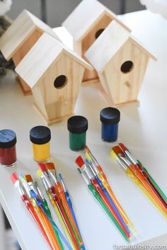 several wooden birdhouses with paint and pencils next to them on a white table