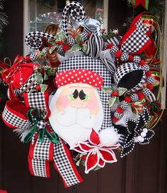 a christmas wreath with santa claus on it and red, black and white bows hanging from the front door