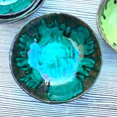 three bowls sitting on top of a wooden table covered in blue and green glaze