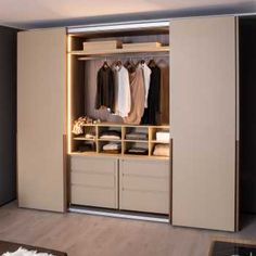 an open closet with clothes on hangers and shoes in the bottom drawer, next to a coffee table