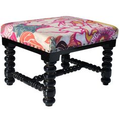 an upholstered foot stool with black legs and colorful fabric on it's seat