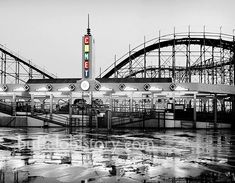 a black and white photo of a roller coaster at an amusement park in the rain