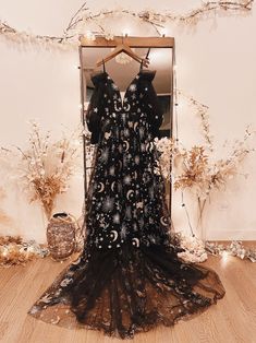 a black dress is on display in front of a mirror with flowers and branches around it