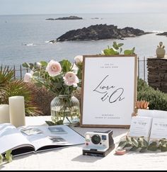 a table with flowers, books and an open book on it next to the ocean