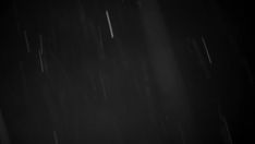 a black and white photo of rain falling down on the ground in the night sky