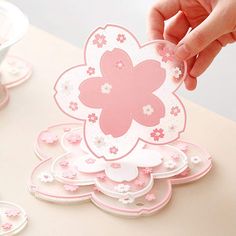 a hand holding a pink flower shaped card on top of a table with plates and cups