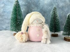 a small stuffed animal sitting in the snow next to some christmas trees and pine cones