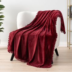 a white chair with a red blanket on it and a potted plant in the background