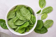 a white bowl filled with green leaves on top of a table