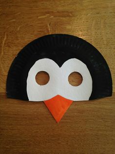 a paper plate penguin mask on top of a wooden table