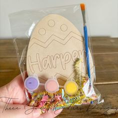 a hand holding a bag filled with crafting supplies and an egg shaped sign that says happy