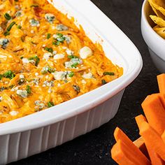 a casserole dish with cheese and vegetables next to some tortilla chips