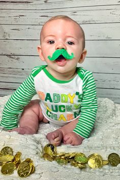 a baby with a fake moustache on his face sitting next to some gold coins