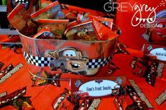 cars birthday party favors and candy bar wrappers on an orange tablecloth with red checkered table cloth