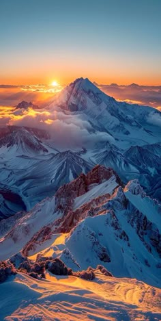 the sun is setting on top of a snowy mountain with snow covered mountains in the foreground