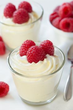 raspberries and whipped cream in small bowls with spoons next to them on a white surface