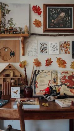 a wooden desk topped with lots of books next to a wall covered in fall leaves