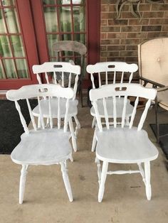 four white wooden chairs sitting in front of a brick wall and red door with glass windows