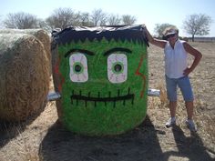 a man standing next to a large green trash can in the middle of a field