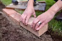 a man is working with bricks in the grass and dirt on the ground while holding his hands over them