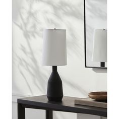 a black table lamp sitting on top of a wooden table next to a white wall