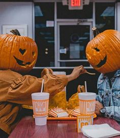 two people sitting at a table with pumpkins on their heads and drinks in front of them