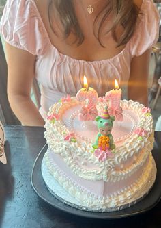 a woman sitting in front of a cake with two lit candles on top of it