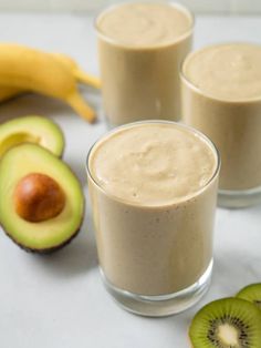 three glasses filled with smoothie next to sliced bananas and an avocado