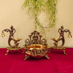 two golden candlesticks sitting on top of a red table cloth next to a potted plant