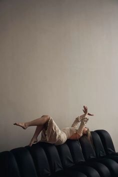 a woman laying on top of a black couch with her legs spread out in the air