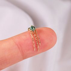 a person's finger with a gold ring on it and a green bead in the middle