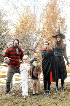 a family dressed up for halloween standing in front of a tree with leaves on the ground