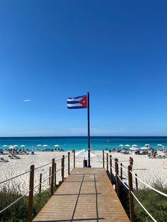 a wooden walkway leading to the beach with umbrellas and chairs in the sand behind it