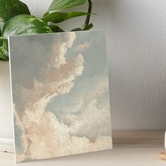 an abstract painting with white clouds and blue sky art boarder on a table next to a potted plant