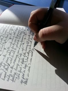 a hand holding a pen writing on top of a piece of paper with cursive writing