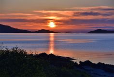 the sun is setting over an ocean with mountains in the distance and water on either side