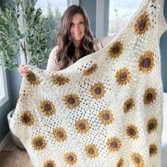 a woman holding up a crocheted sunflower blanket