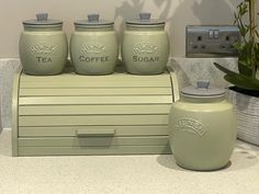 four green canisters sitting on top of a counter next to a potted plant