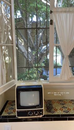 an old fashioned tv sitting on top of a counter next to a window with curtains