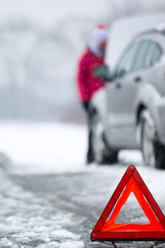 a red triangle sign sitting on the side of a road next to a white car