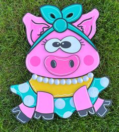 a pink and blue pig sitting on top of green grass next to a frisbee