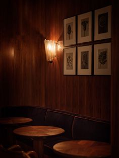 some tables and chairs in a room with pictures hanging on the wall above them at night