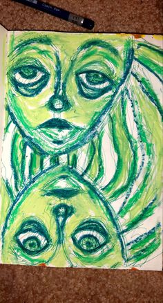 a drawing of two faces with green hair and eyes on paper next to a marker pen