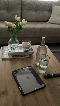 a table topped with a tablet computer next to a glass vase filled with white flowers