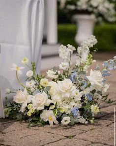 a bouquet of white and blue flowers on the ground next to a chair at a wedding