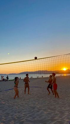 people playing volleyball on the beach at sunset