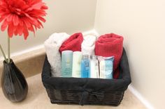 a black basket filled with personal care items next to a red flower in a bathroom