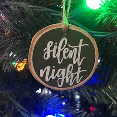 a wooden ornament that says silent night hanging from a christmas tree with lights in the background