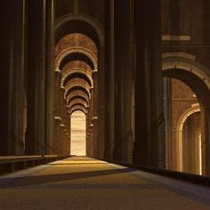 an empty hallway with arches and light at the end